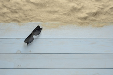 Gafas de sol de color negro y arena sobre fondo de madera azul