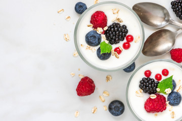 healthy yogurt with fresh forest berries in glasses with spoons on white marble background. healthy diet breakfast