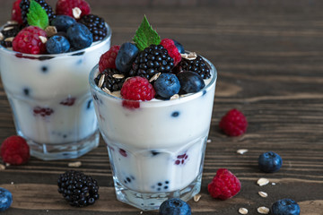 greek yogurt with fresh berries, oats and mint in glasses on rustic wooden background. healthy diet breakfast
