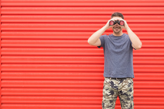 Modern Man Looking Through Binoculars Against Red Metal Wall.