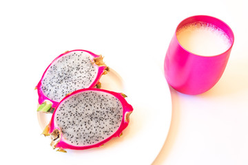 Cut dragon fruit on a white plate, pink cup of milk, horizontal aspect