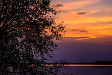 colorful sunset by the lake with trees and red sky in background