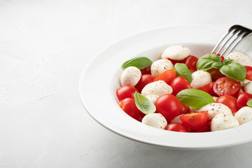White plate of classic delicious caprese salad with ripe tomatoes, mozzarella and fresh basil leaves on gray background with copy space. Italian food. The concept of a healthy vegetarian diet