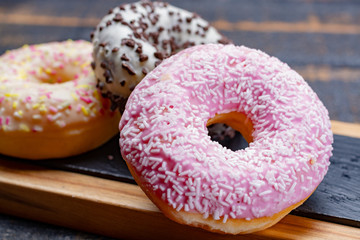 Colorful sweet glazed donuts from bakery on black wooden background close up