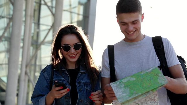 Happy Couple Travelling to Foreign City. Walking near the Airport. Young Attractive Woman Using her Mobile Device. Handsome Man Browsing Tourist Map. Looking for Direction. Casully Dressed.