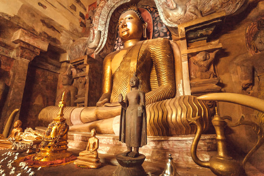 Golden sculpture of meditating Buddha inside cave of stone temple. Buddhist structure with sculptures from 14th century, Sri Lanka