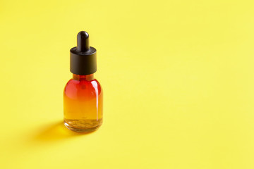 Glass bottle for cosmetics, serums and oils with a pipette on a yellow background.