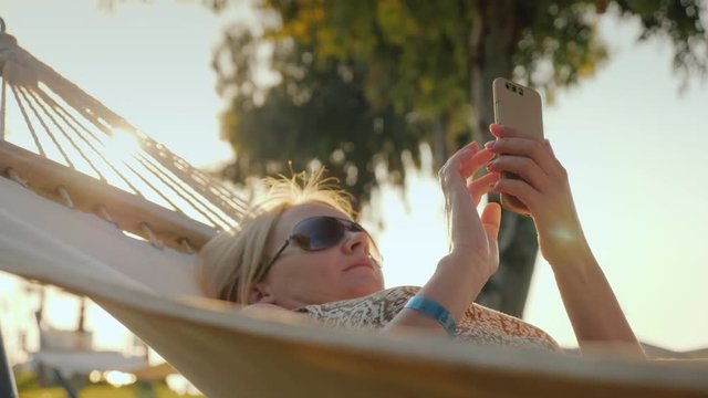A woman uses a smartphone on vacation, relaxes in a hammock in the early morning