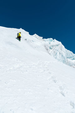 A skier in a helmet and mask with a backpack rises on a slope against the background of snow and a glacier. Backcountry Freeride