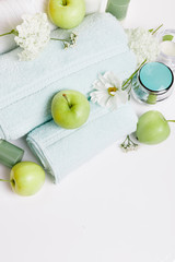 Spa setting on white table. Green apples, towels, cosmos flowers and hydrangeas, cosmetics, candles. Spa resort therapy composition, spa summer concept. Top view