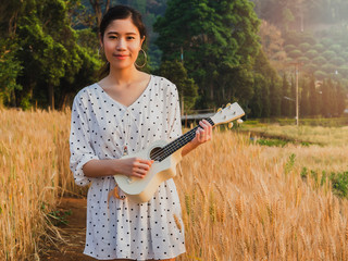 Asian woman with ukulele in barley field at sunset time