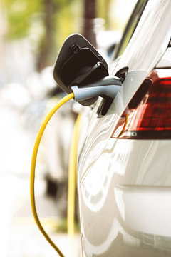 Modern electric car charging with power cable in the city street. Green urban transport mode