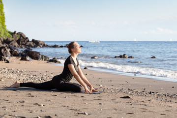 Fototapeta na wymiar Young woman in black doing yoga on sand beach