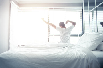 Man wake up and stretching on bed in morning with sunlight - obrazy, fototapety, plakaty