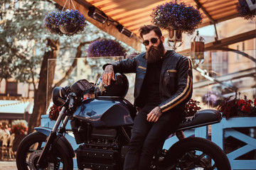 Stylish fashionable biker in sunglasses dressed in a black leather jacket, sitting on his...