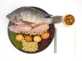 healthy natural food and diet concept - high protein many beans and meat, red beans, green beans, soy beans, egg, chicken and fish in the brown dish on white background with book and pen