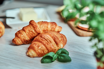 Photo of a croissant with ham and cheese on wooden board.