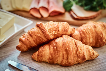 Close-up photo of a croissant with ham cheese and butter on wooden board in a kitchen.