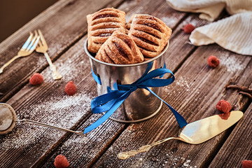 Close-up photo of a puff pastry with jam in a bucket decorated with a blue ribbon on wooden boards with raspberries and cutlery.