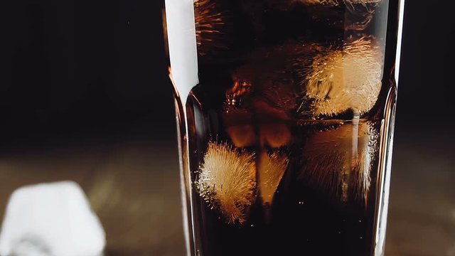 Cola with ice cubes and bubbles in glass, slow motion.