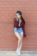 Asian hipsters girl  on orange brick wall,lifestyle of modern teenage,Happy lady posing for take a photo,thailand people Wearing a plaid shirts and jeans shorts.