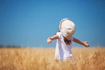 Happy girl walking in golden wheat, enjoying the life in the field. Nature beauty, blue sky and field of wheat. Family outdoor lifestyle. Freedom concept. Cute little girl in summer field