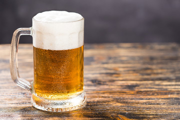 Mug of cold pale beer placed on a rustic wooden table with copy space.