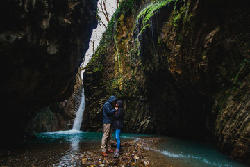 Romantic couple in mountains. Man and woman standing and hugging near waterfall. Active lifestyle in nature.
