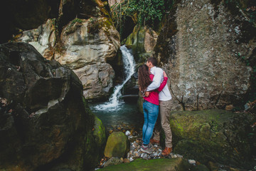 Romantic couple in mountains. Man and woman standing and hugging near waterfall. Active lifestyle in nature.