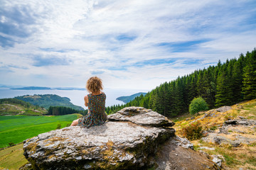 Woman watching over the fjord in Norway, near Nedstrand in Rogaland. Sitting on a stone with trees and water in front