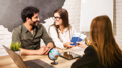 Young lovely couple sitting with manager at the travel agency office prepairing for a summer...