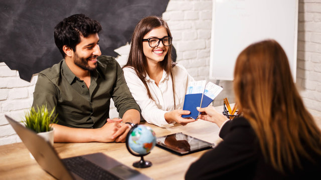 Young cute couple choosing a trip with agent sitting at the travel agency office with world map on the background
