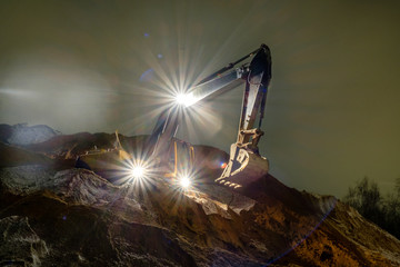 The yellow excavator works at night in the headlights and additional lights. Loads of sand. Night shooting.