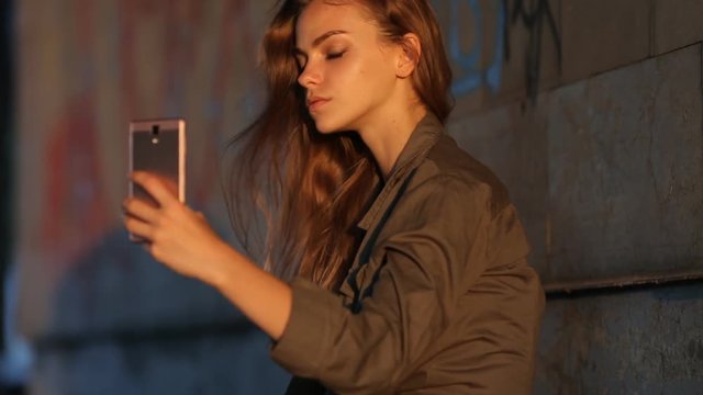 Video portrait of an attractive Caucasian white girl with beautiful hair. Happy girl in the underpass makes selfi on the smartphone.