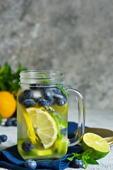 Lemonade with lime, lemon and blueberries on a stone background. Summer cold drink.