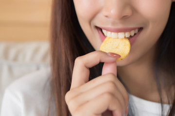 happy, smiling woman eating potato chips or crispy fried potato; unhealthy food or fried food...