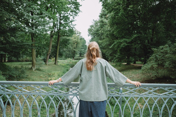 Young woman relaxing in summer green park , posing on bridge , back view