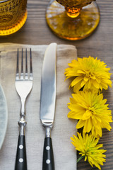 Rustic table setting with linen napkin, cutlery, ceramic plates, yellow glasses and yellow flowers