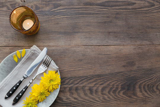 Rustic table setting with linen napkin, cutlery, ceramic plates, yellow glasses and yellow flowers