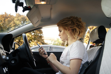 Business woman sitting in car and using her smartphone. Mockup image with female driver and phone screen