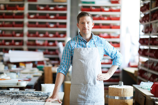 Waist up portrait of modern artisan wearing apron standing  confidently and  looking at camera while posing in workshop, copy space