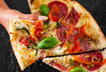 woman Hand takes a piece of Pizza with Mozzarella cheese, Ham, Tomatoes, salami, pepper, pepperoni, Spices and Fresh Basil.