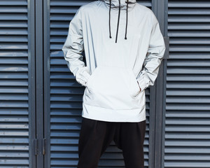 New, modern material in the fashion industry. Windbreaker from the rain. A young man posing in a fashionable silvery waterproof jacket on a metallic background. Part of the body.