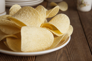 Many potato chips in round plate isolated on rustic wooden table and black background. Snack food.