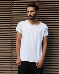 Fashion of the young. A man in a white T-shirt posing on a rusty metal background in the summer evening. Cover.