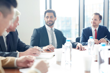 Jolly confident handsome mixed race businessman with beard leading discussion with colleagues at meeting in conference room