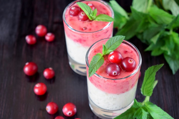 Two layered smoothie in glasses surrounded by cranberries and mint against the dark background