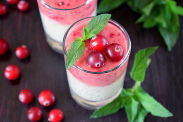 Two layered smoothie in glasses surrounded by cranberries and mint against the dark background