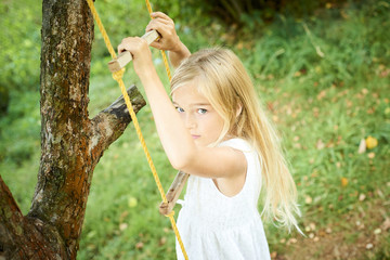 A child cute girl swinging on a rope ladder in summer in the garden