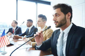 Serious handsome young mixed race politician with beard participating in debate and talking into...